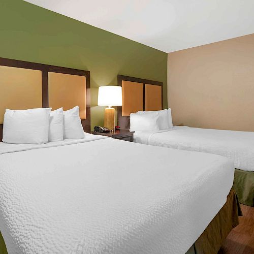This image shows a hotel room with two double beds, white bedding, a nightstand with a lamp, and a green and brown color scheme on the walls.