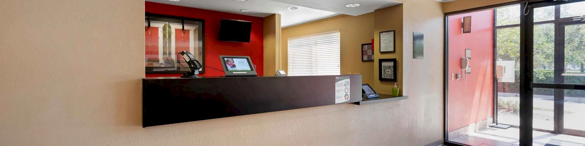 This image shows a reception desk area with a computer, some framed pictures, and a glass entrance door to the right.