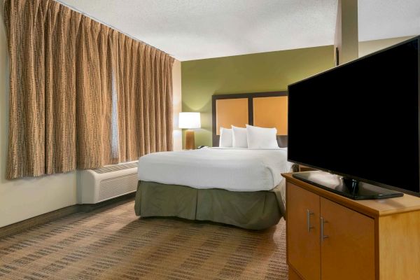 A hotel room with a large bed, bedside lamp, curtains, carpeted floor, and a TV on a cabinet, ending the sentence.