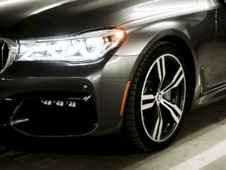 The image shows a close-up of a sleek, dark-colored car parked in a parking garage, highlighting its stylish alloy wheels and headlights.
