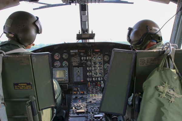 Two pilots are seen from behind in the cockpit of an aircraft, with various dials and controls visible.