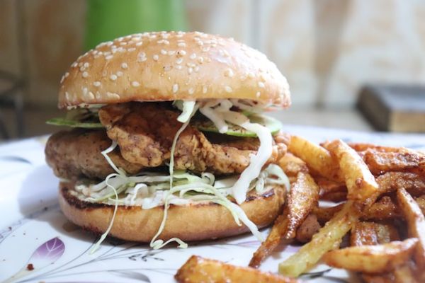 A fried chicken sandwich with lettuce and cabbage, accompanied by crispy French fries on a decorative plate, is shown in this image.
